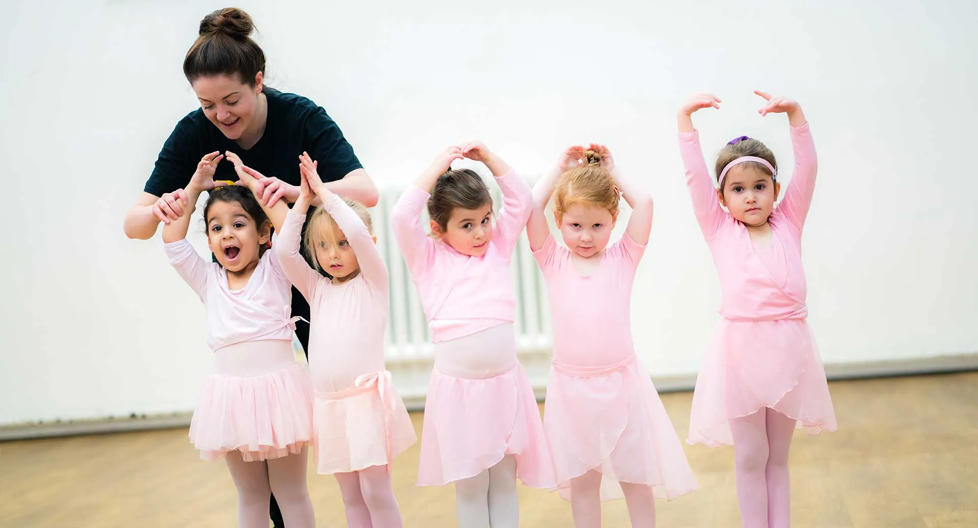Young girls in pink tutus practising ballet poses with their teacher